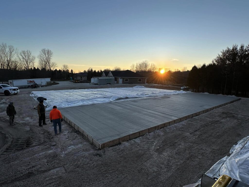 Workers finishing freshly poured concrete slab at sunset